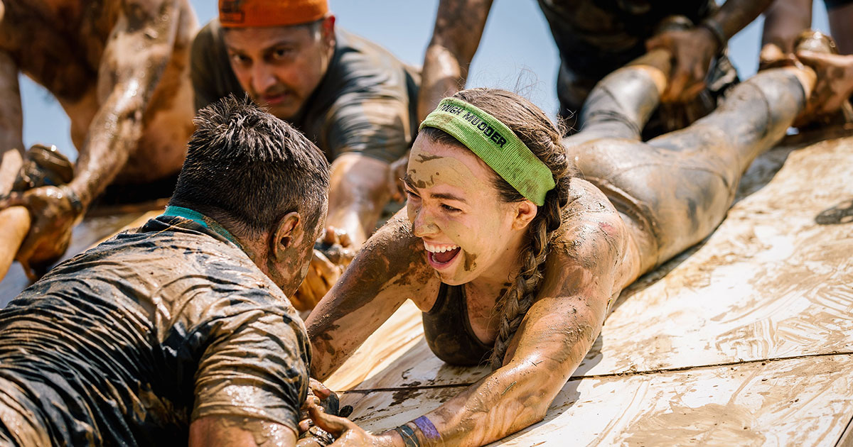 Participant smiling while holding the hand of her teammate to help him climb