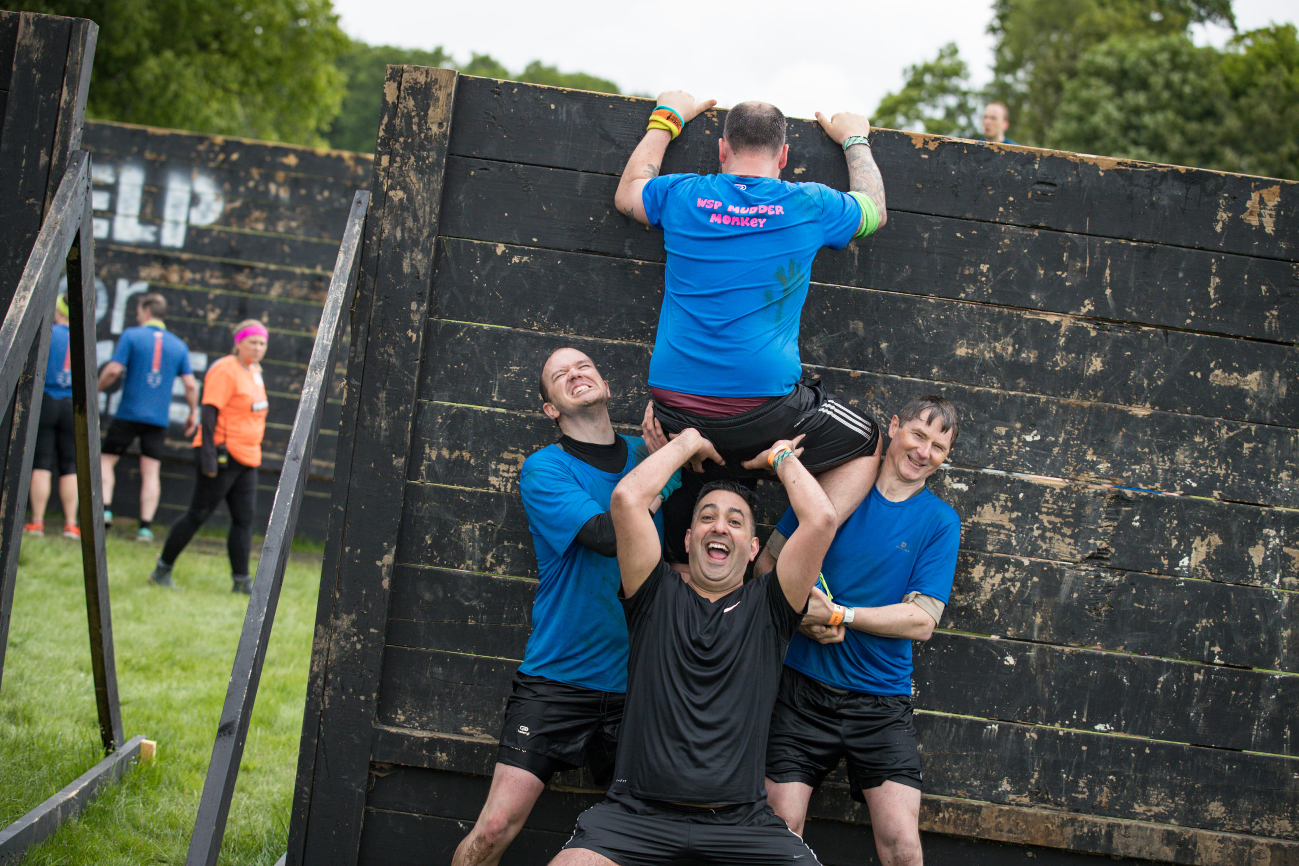Three men trying to push a man over a wall