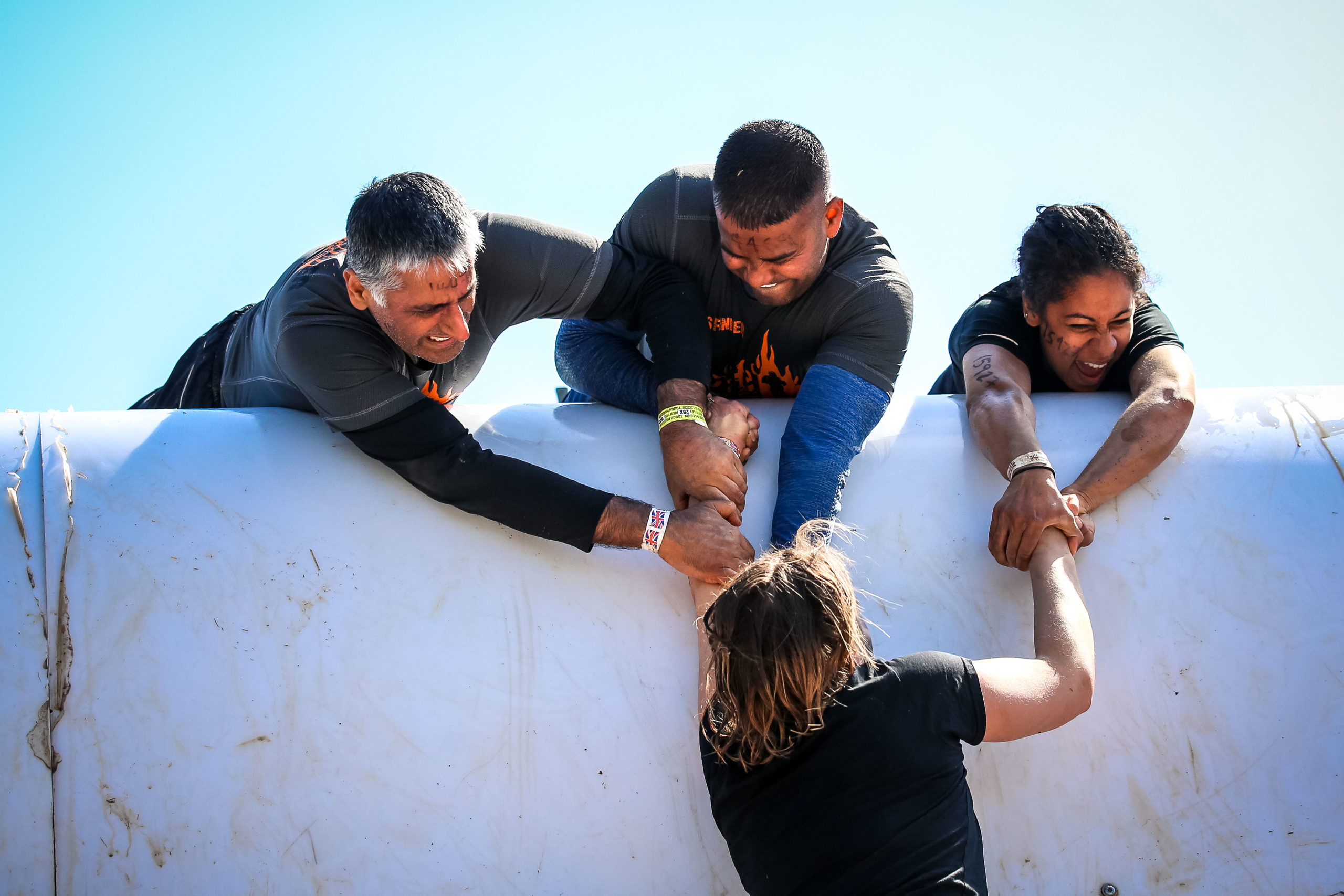Three participants helping their one teammate by pulling her up