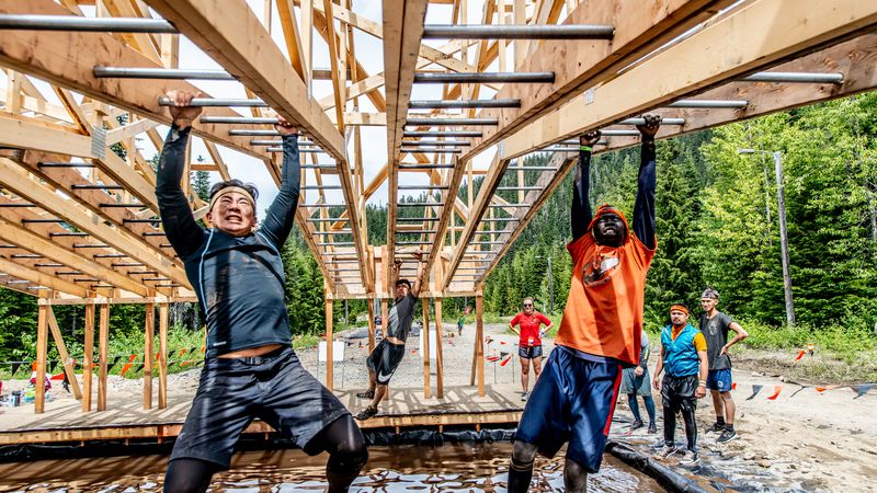 Two men swinging on Tough Mudder monkey bars